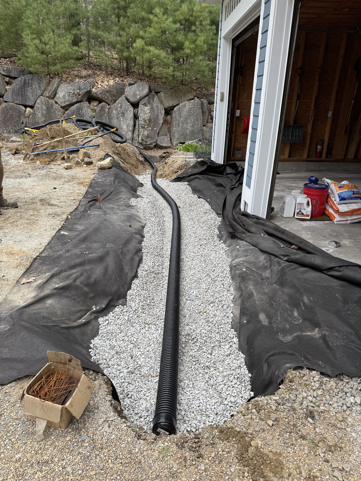 Corrugated perforated drain pipe laid in crushed stone over geotextile before backfilling — GSS drainage, Seacoast NH